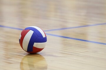 red, white, and blue volleyball on an indoor wood court
