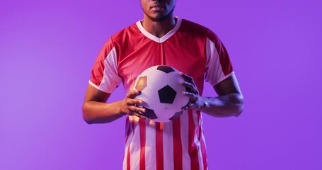 Portrait of african american male soccer player with football over neon pink lighting - Powered by Adobe