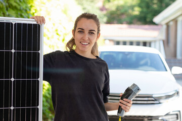 Portrait of young woman holding a solar panel showing the source of energy for her electric white...