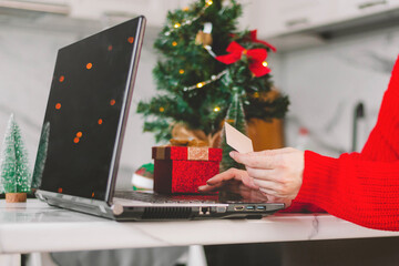 Woman holds a credit card and gift in her hands opposite the laptop. Online shopping. Valentine's Day gifts. 14 February New Year on COVID-19 pandemic. Home delivery. Shopping online during holidays.