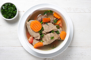 Sup daging, clear soup with beef slices, and vegetables, Served in a bowl.