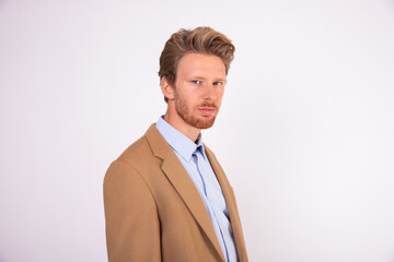 Confident young Caucasian businessman looking at camera. Portrait of bearded man beige woolen suit coat standing against white background. Successful businessman concept