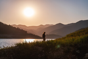 Fototapeta na wymiar Woman traveler admiring the sunset on the shore of a lake in the mountains. Tara National Park Serbia