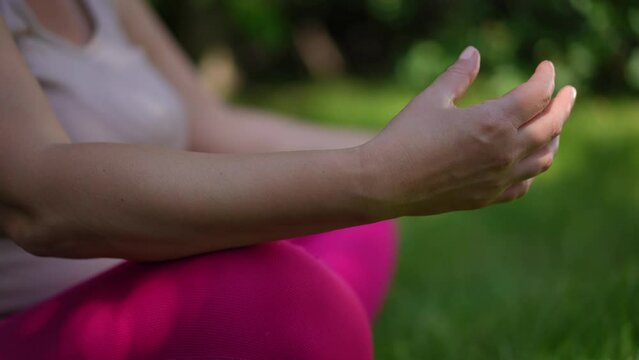 Close-up hand of overweight woman sitting lotus pose meditating outdoors. Unrecognizable Caucasian plus-size yogi exercising in summer park outdoors side view. Tranquility and life balance