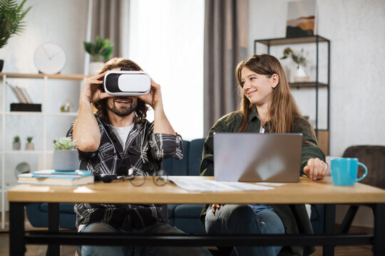 Excited young people with surprised expression, playing games at home and using VR glasses and laptop. Happy man wears VR headset, while pretty girl uses laptop and smiles
