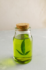 Cannabis CBD hemp oil in a glass bottle with a green leaf on a gray background. The concept of Alternative Oil. Vertical orientation.