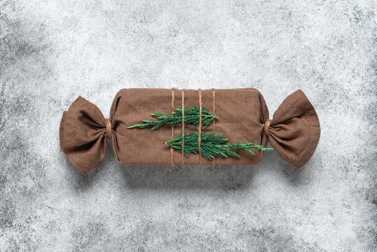Christmas gift wrapped in fabric with green branches, gray rustic background. Gift in furoshiki style. Zero waste concept. Top view, flat lay. Selective focus.