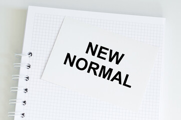 Word Text NEW NORMAL on a card that sits on a notebook on a table, a medical concept