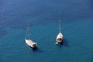 Aerial view to yachts with the sails lowered on blue sea surface. Two sailboats lying at anchor,...