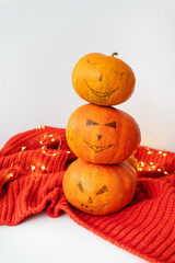 Three pumpkins with a painted face on a red sweater. The concept of the holiday on October 31, Halloween. Nice bokeh in the background.