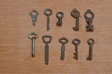 ten old different iron small rusty keys from doors and locks lie on a beige wooden surface