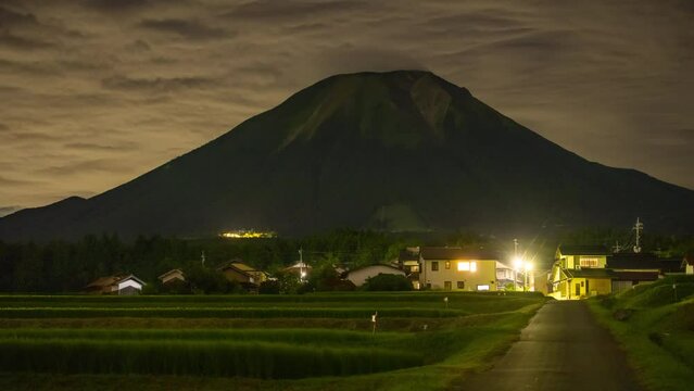 Night Timelapse: Country road leads to lit houses at foot of Mt. Daisen as clouds move overhead