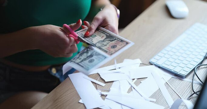 Counterfeiter cuts dollar bills with scissors at table closeup