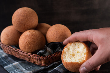 Hand taking a round colombian traditional food named buñuelo in a basket on black wooden table 