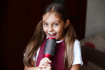 Beautiful brunette little girl singing in brush at home. Kid enjoying singing hairbrush mic.