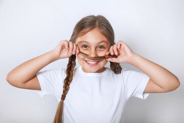 Cheerful happy little kid girl in white t-shirt makes a mustache from her hair on white studio background.