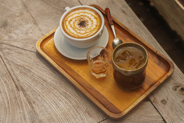 hot caramelmachiato in a white ceramic cup and honey in a glass and water in a ceramic glass and wooden spoon, place on a rectangular wooden tray,  on the wooden table 