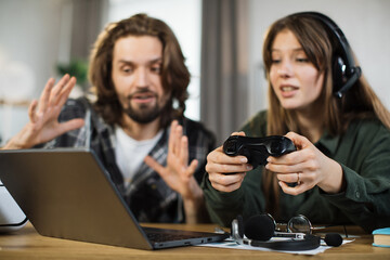 Waist up portrait of happy young people, handsome man and pretty blond woman, sitting and embracing together, playing video games using wireless joystick. Promo ad of family video games leisure.