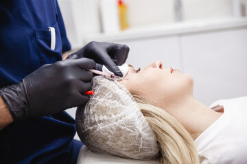A cosmetologist in black gloves injects botulinum toxin into the patient's forehead. A blonde...