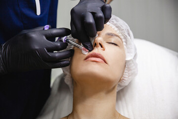 The doctor cosmetologist in black gloves makes Lip augmentation procedure of a european woman in a beauty salon. 