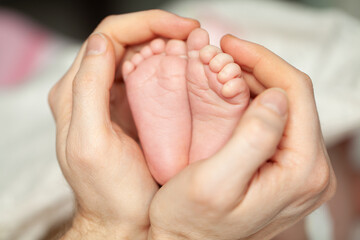 Man's strong hand gently holds little feets newborn