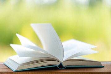 Open book on wooden table on natural background. Concept of reading books. Wind turns the pages. Image with shallow depth of field.