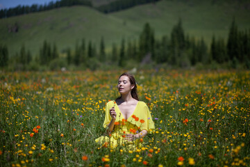 A girl in a yellow dress walks in a flowering field. The field blooms in the mountains