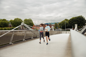 Two athletic women in sportswear is jogging on a bridge and listening music. Reaching the goal