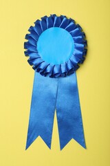 Blue award ribbon on yellow background, top view