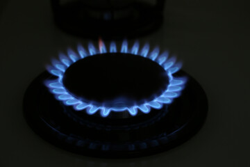 Gas burner of modern stove with burning blue flame at night, closeup