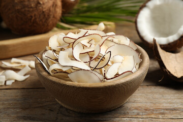 Tasty coconut chips in bowl on wooden table