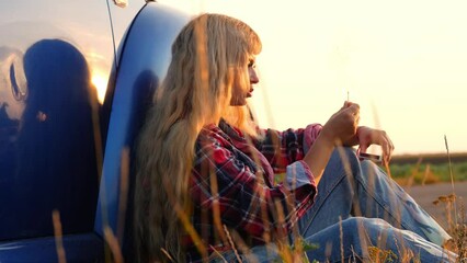romantic road trip concept, young woman traveller sitting on the road near the car at sunset, burning matches, freedom and adventure concept