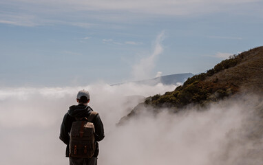 Young man with a tourist backpack watching a scenic landscape of mountains and clouds, hiking in Madeira