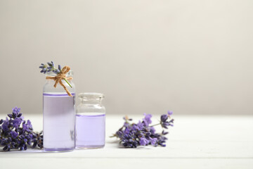 Bottles of essential oil and lavender flowers on white wooden table. Space for text