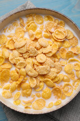 Bowl of tasty corn flakes on light blue wooden table, top view