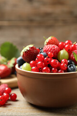 Mix of different fresh berries in bowl on wooden table