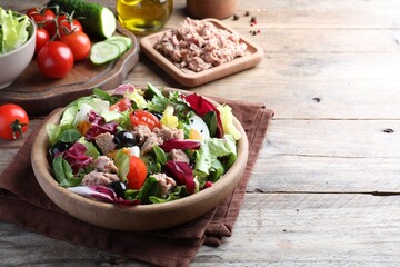 Bowl of delicious salad with canned tuna and vegetables on wooden table, space for text