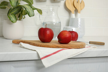Clean towel and wooden board with ripe apples on countertop in kitchen