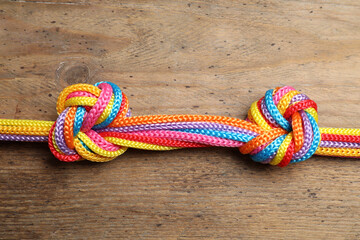 Colorful ropes tied together on wooden background, top view. Unity concept