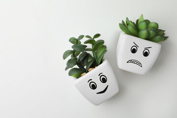 Top view of beautiful potted houseplants with angry and happy faces on white background, space for...