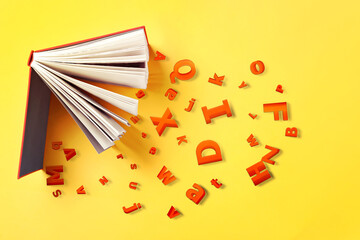 Open book with letters on yellow background, flat lay. Dyslexia concept