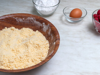 Mixed butter with flour in bowl. On the table are eggs, raspberries, powdered sugar in glass bowls. Selective focus. Image for articles about food, sweets.