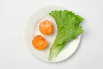Tomatoes and lettuce leaf on a white plate on a light background. View from above. Flat lay.