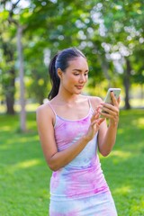 Young asian woman doing mobile banking on her smartphone in a park. Business on the go.