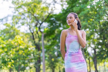 Portrait photo of the beautiful moment of a young asian beautiful lady happily talking on her phone with her friends during a garden park strolling
