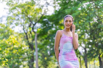 Portrait photo of the beautiful moment of a young asian beautiful lady happily talking on her phone with her friends during a garden park strolling