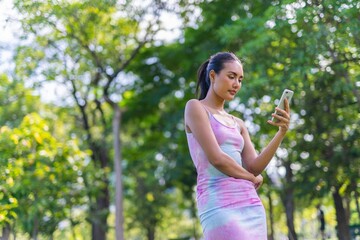 Portrait photo of the beautiful moment of a young asian beautiful lady happily chatting on the app in her smartphone with her friends during a garden park strolling