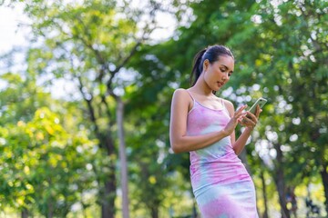 Portrait photo of the beautiful moment of a young asian beautiful lady happily chatting on the app in her smartphone with her friends during a garden park strolling