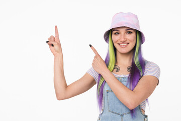 Obraz na płótnie Canvas Cheerful caucasian hipster young girl woman with dyed colorful hair in cap pointing showing copy space free space isolated in white background