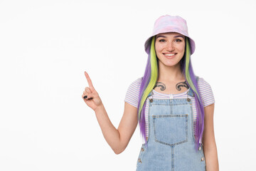 Fototapeta na wymiar Smiling with toothy smile young caucasian teenage hipster girl woman with bright colorful dyed hair and tattoo pointing with finger at copy space isolated in white background